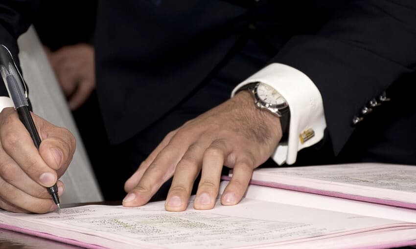 Manos firmando un documento sobre un escritorio